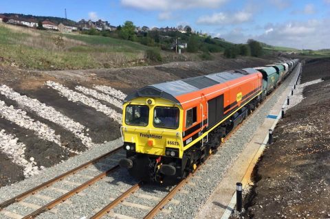 Freightliner class 66 diesel in orange livery pulling away from Buxton quarry in the English Peak District