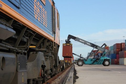 iPortRail reach stacker loading an intermodal train as seen from the cab side of the locomotive