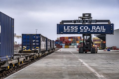 Tesco container with "Less CO2" logo being loaded by reach stacker onto an intermodal train at Granegmouth