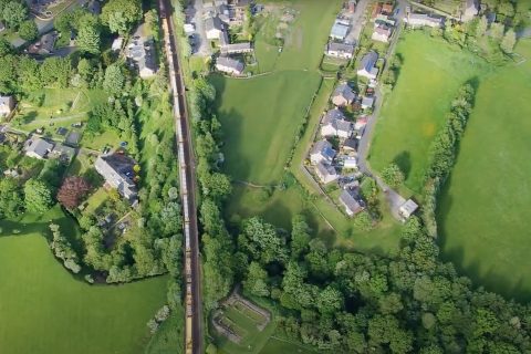 Overhead shot of a long freight train travelling through village and countryside