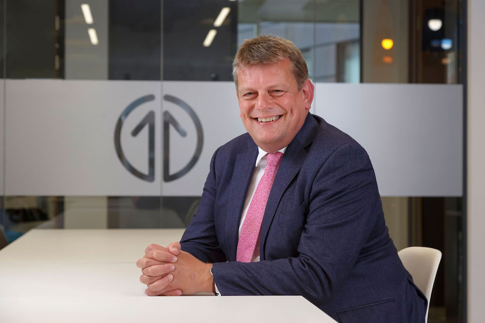 Portrait of Martin Tugwell, chief executive of Transport for the North, seated in office with TfN logo in window