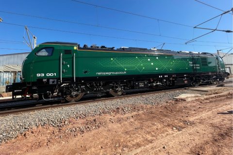Class 93 tri-mode locomotive in racing green livery under a blue sky on rails with red earth in foreground