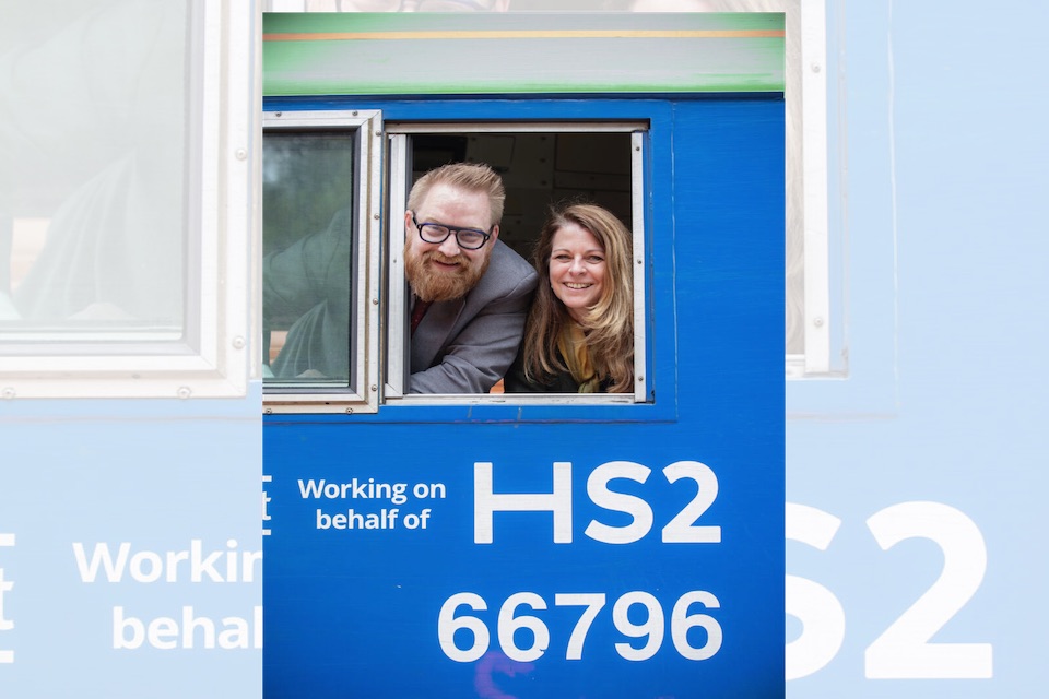 HS2 personnel smiling out of the cab window of a class 66 locomotive with the wording "working on behalf of HS2"