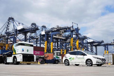 A ground level image of a clean fuel electric car and a tractor in front of dock cranes at Hutchison's Port of Felixstowe