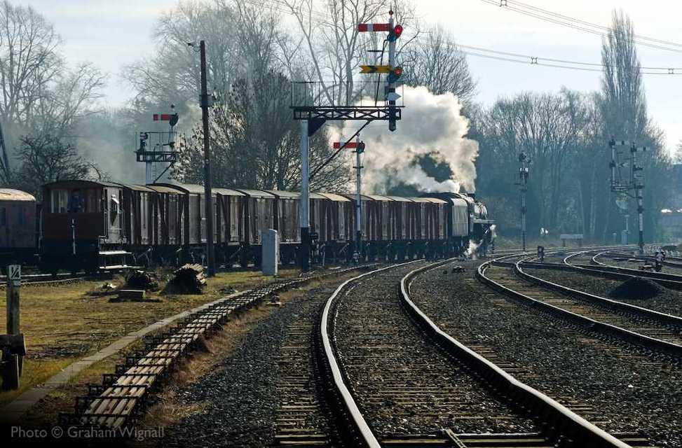 Steam locomotive drawing away from the camera with a goods train on the Great Central Railway, under double semaphore signals