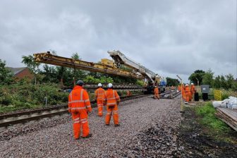 Yellow rail crane arrives on site at Ashington to help install new points for the upgrade project. Engineers in orange suits watch on