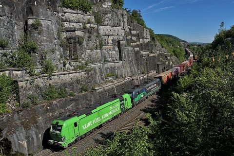 Image of intermodal train in deep gorge in Bavaria being hauled by bright green locomotive