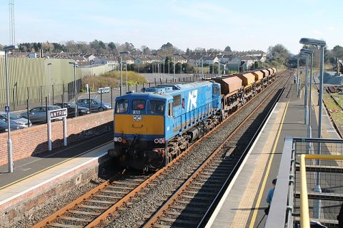 An engineering train hauling ballast trucks passes Antrim station in Northern Ireland seen from an elevated position above the tracks