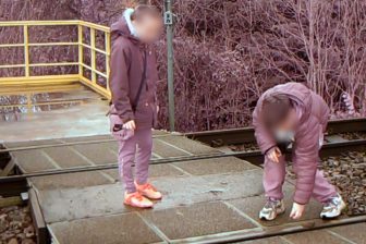 Two children stand on a level crossing placing ballast stones on track