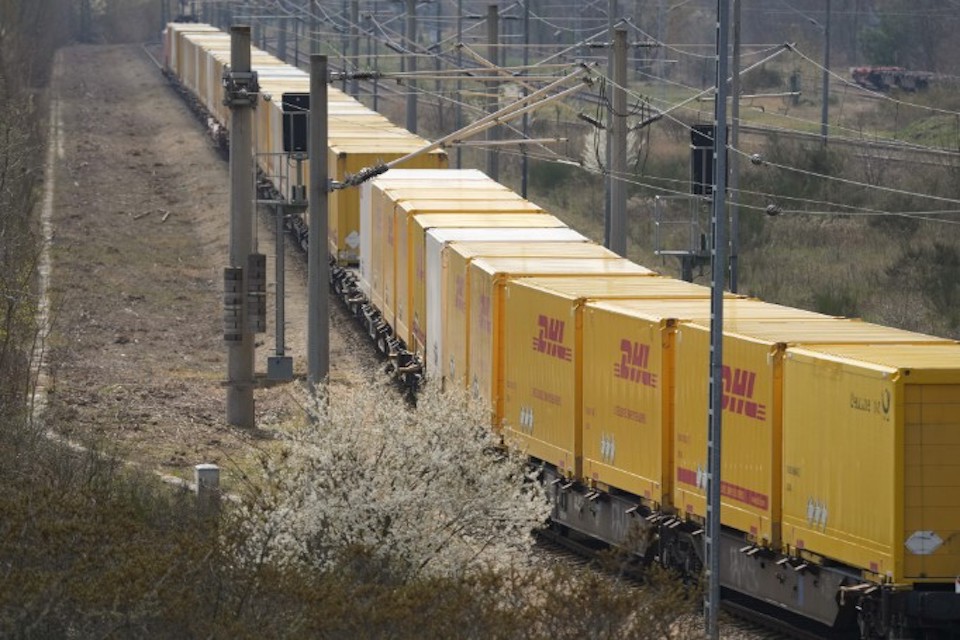 Long train of intermodal containers all liveried in DHL yellow and under the wires