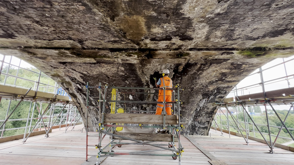 Orange suited Engineer working from a scaffolding platform under one of the arches of Sankey Viaduct
