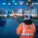 In a high visibility jacket, an inspector from the Office of Rail and Road stands with his back to the camera supervising evening intermodal operations