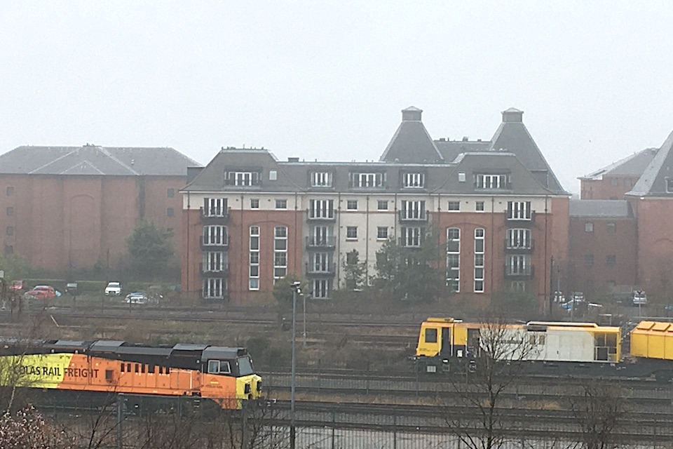 A misty day in Edinburgh with a residential block behind orange and yellow Colas locomotives and engineering vehicles