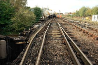Track level image of damaged tracks with derailed wagons in background