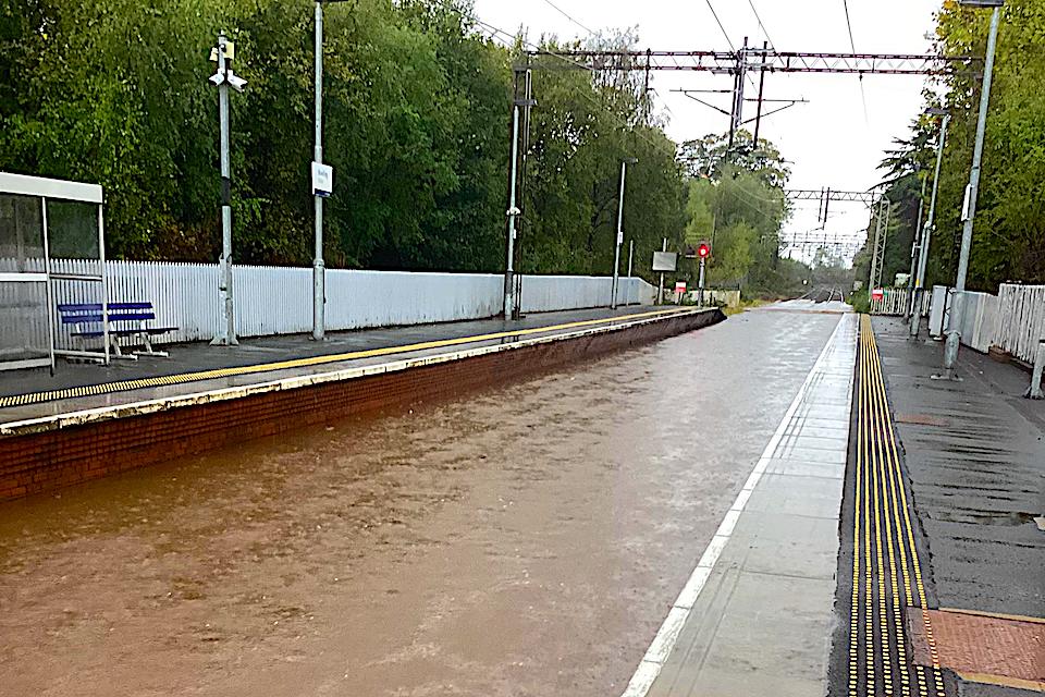 Brown coloured flood water drowns the tracks and flows though Bowling station in the west of Scotland - water is up to platform level