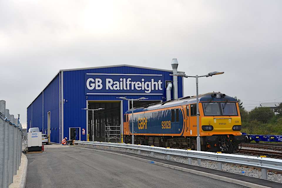 Ground level shot of GB Railfreight maintenance hub in Peterborough with locomotive standing outside and GBRf logo in white on the blue building