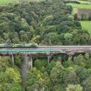 Aerial shot of triple headed engineering train on PLessey Viaduct in Northumberland, England, showing a wooded scene over a deep river valley