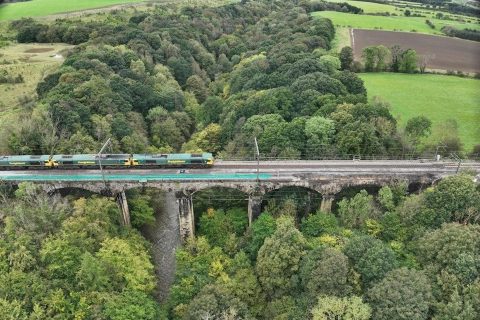 Aerial shot of triple headed engineering train on PLessey Viaduct in Northumberland, England, showing a wooded scene over a deep river valley
