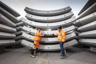 Two engineers standing in front of a stack of huge prefabricated tunnel segments