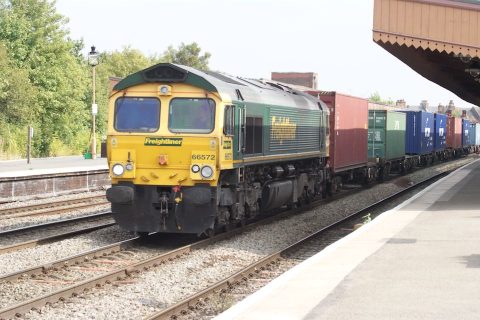 A Diesel hauled container train hurries through a small stain, as seen from the platform