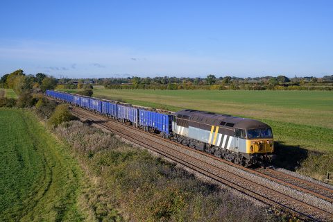 Class 56 diesel locomotive in a grey livery working a train of blue open wagons in a countryside setting